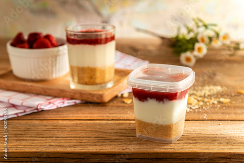 Close up of crispy strawberry cheesecake in plastic containers take away box over a red, white plaid napkin on the table. Food recipe eatable delicious dessert cooked courier delivery product concept