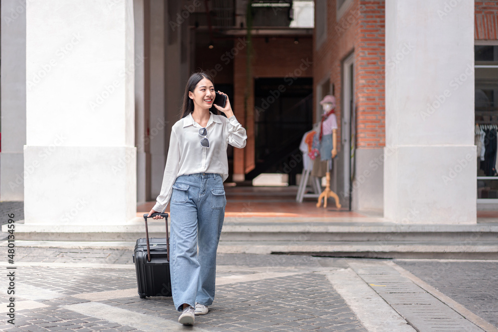 Smiling woman traveller talking using smartphone and dragging black suitcase luggage bag walking to passenger boarding in airport, Travel concept