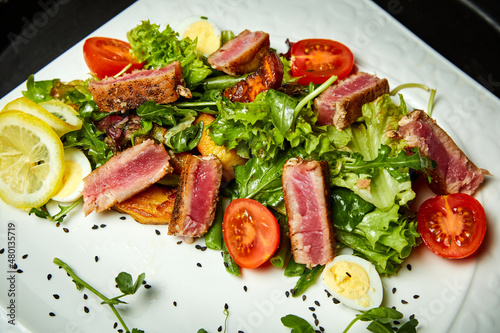 Salad with tuna, mix salad, cherry tomatoes, potatoes and quail egg. Close-up, selective focus.