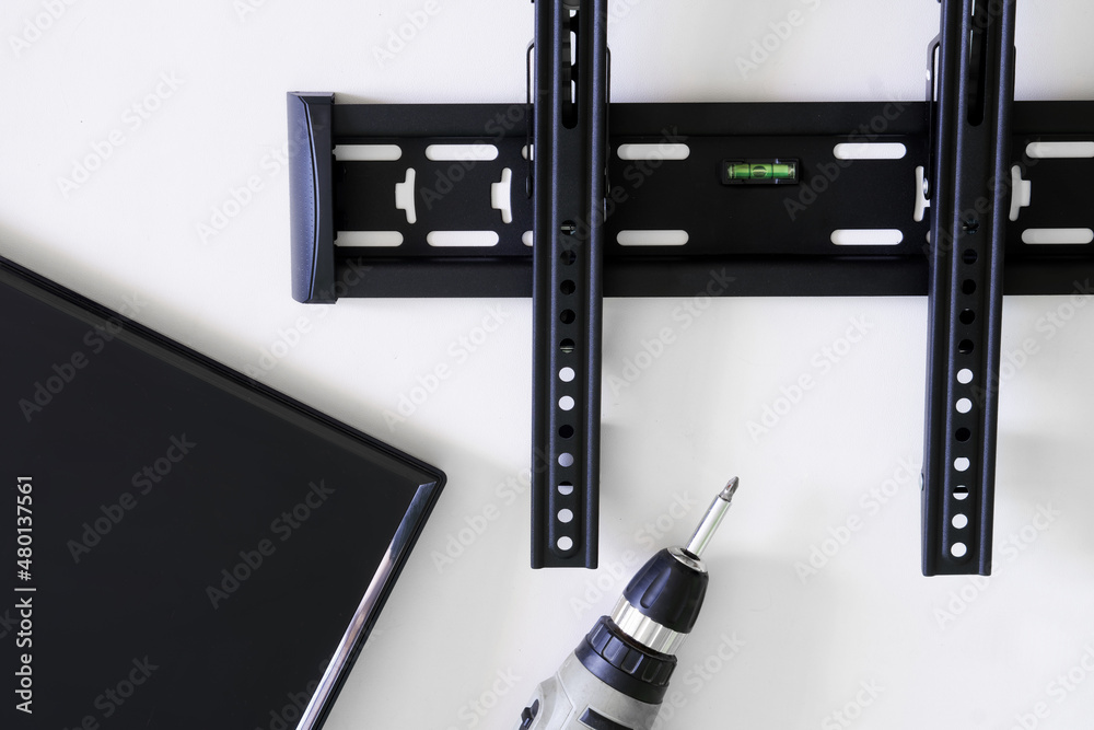 Obraz premium TV wall mount bracket, monitor or TV and electric drill. The concept of mounting a TV or computer monitor on the wall using a bracket. Bubble level