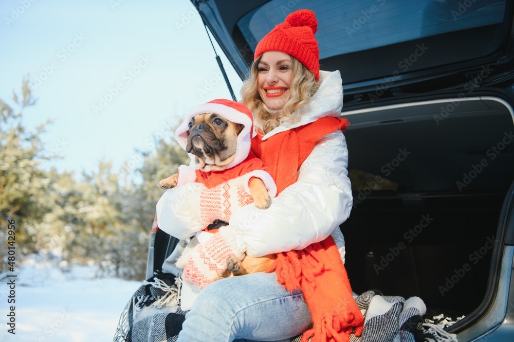 Woman resting in the winter forest sitting in the open trunk of a car with a dog.