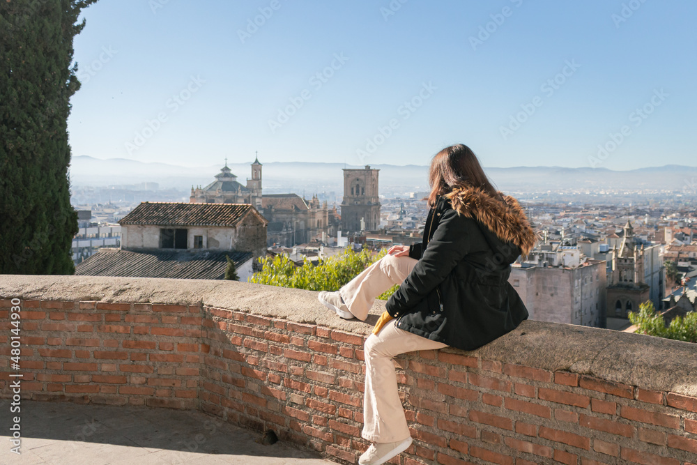 Fototapeta premium Granada old town and the Cathedral. Woman is sitting on the wall and seeing the Granada's views. It's a sunny day in Granada, Andalusia, Spain.