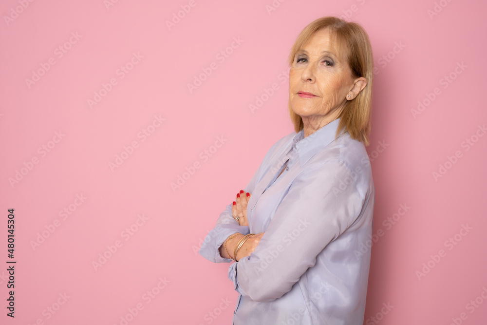 Senior woman posing with arms folded standing isolated over pink background. Senior woman posing with arms folded standing isolated over pink background.