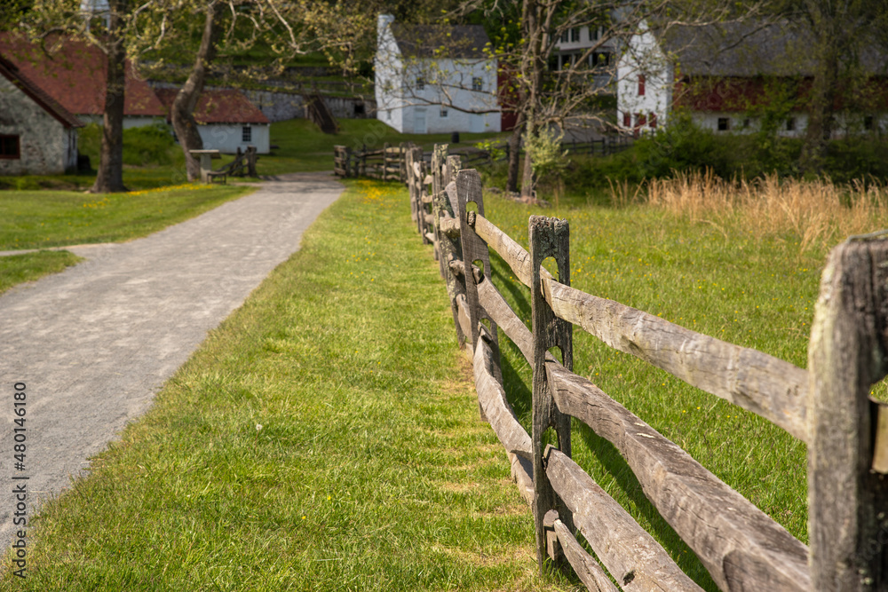 Wooden fence along walking path leads to colonial American village.
