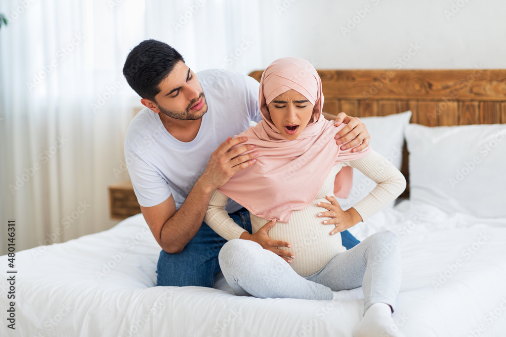 Prenatal contractions. Pregnant muslim woman suffering from abdominal pain and caring arab husband comforting wife Prenatal contractions. Pregnant muslim woman suffering from abdominal pain and caring arab husband comforting wife