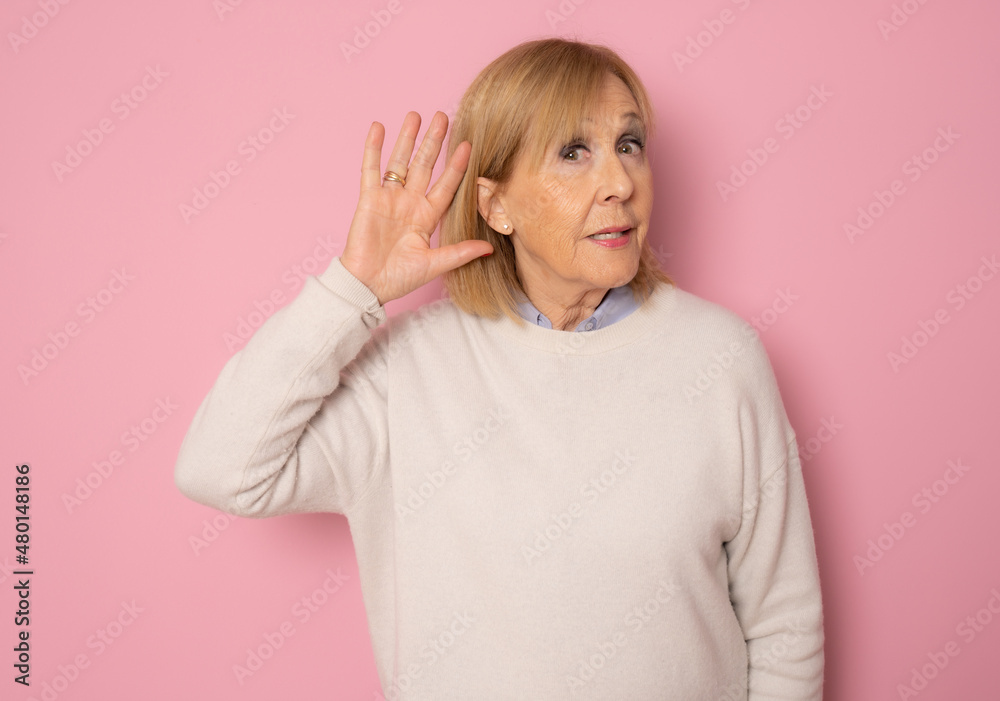 Portrait of cheerful old woman in white sweater making listening gesture, isolated on pink background Portrait of cheerful old woman in white sweater making listening gesture, isolated on pink background