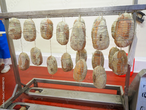 worker hand sewing and finishing culatello, coppa and prosciutto cold cuts in delicatessen manufacturing facility in Parma Italy photo