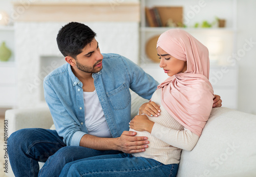 Care in couple during pregnancy. Worried arab husband supporting pregnant wife with prenatal contractions at home