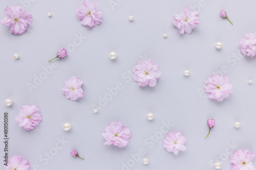 Fresh cherry blossom sakura flowers and white pearls on pastel pink background. Abstract natural floral pattern. Spring concept. Minimalist flat lay, top view