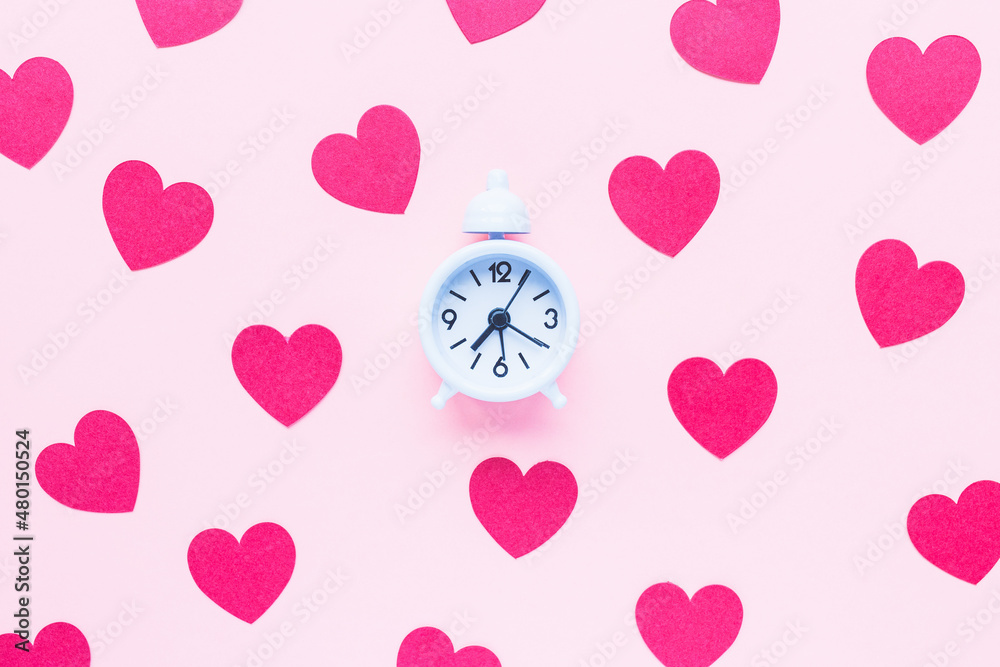 Valentines Day background with small white alarm clock and red hearts on pink. Love, dating, dinner planning and shopping gifts concept. Top view