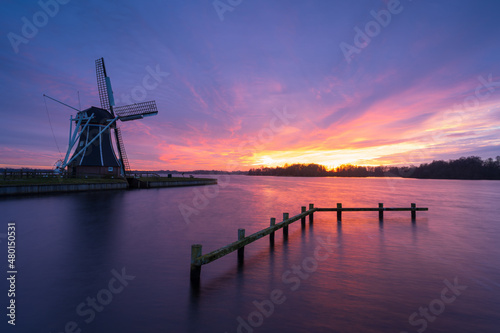 Dutch windmill at a lake during windy and colourful sunset.
