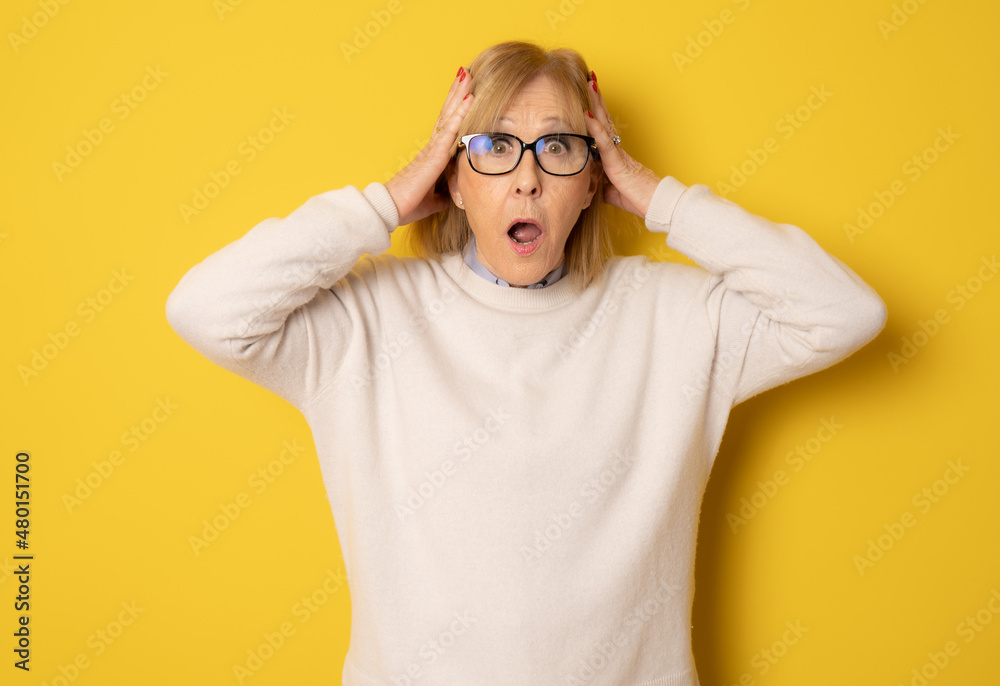 Elderly amazed woman in glasses open mouth gawp look at camera feels stunned isolated on yellow background Elderly amazed woman in glasses open mouth gawp look at camera feels stunned isolated on yellow background