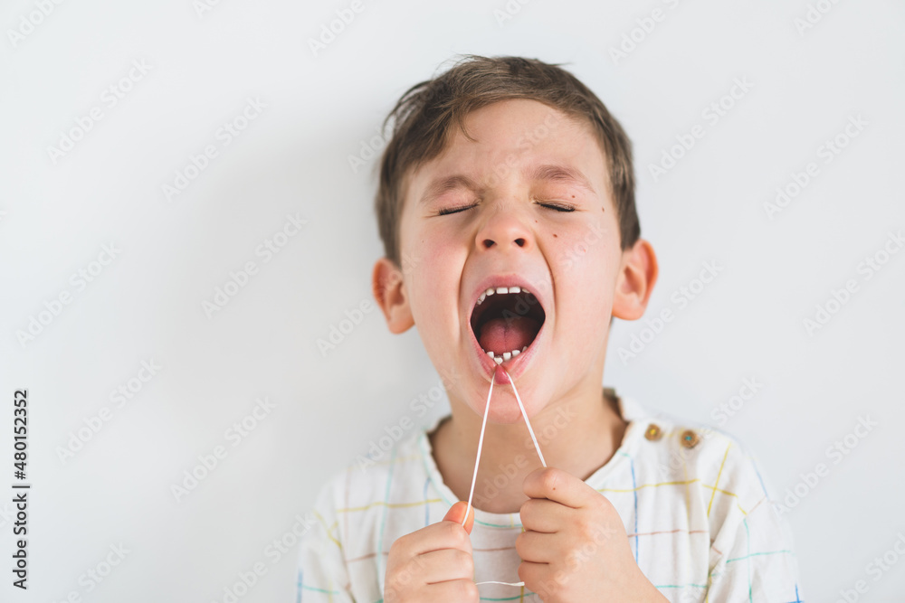 Foto Stock Cute boy pulling loose tooth using a dental floss. The boy's