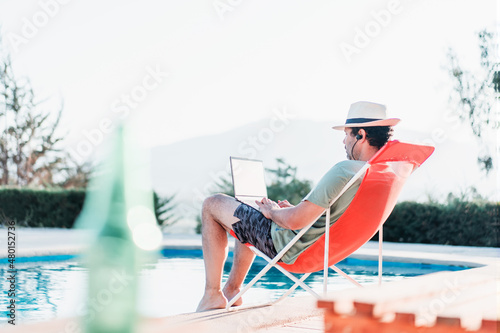 man sitting on beach chair by the swimming pool with a laptop alone