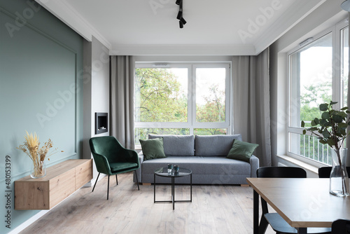 Modern living room in minimal interior with big window  sofa  armchair and green wall. Scandinavian concept for cozy room.
