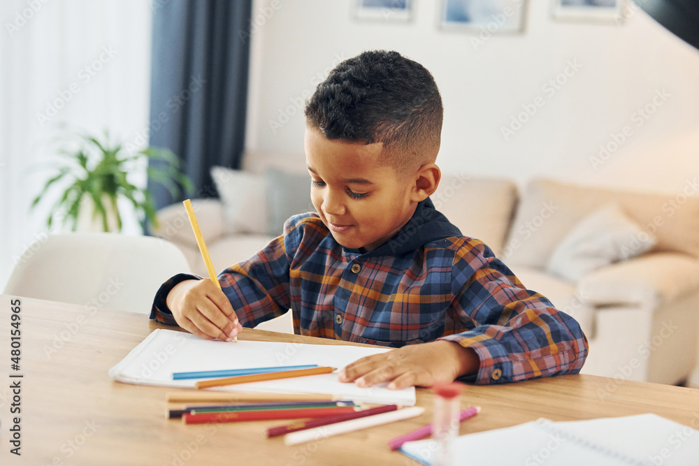 Sitting by the table. Cheerful young boy is at home alone Sitting by the table. Cheerful young boy is at home alone