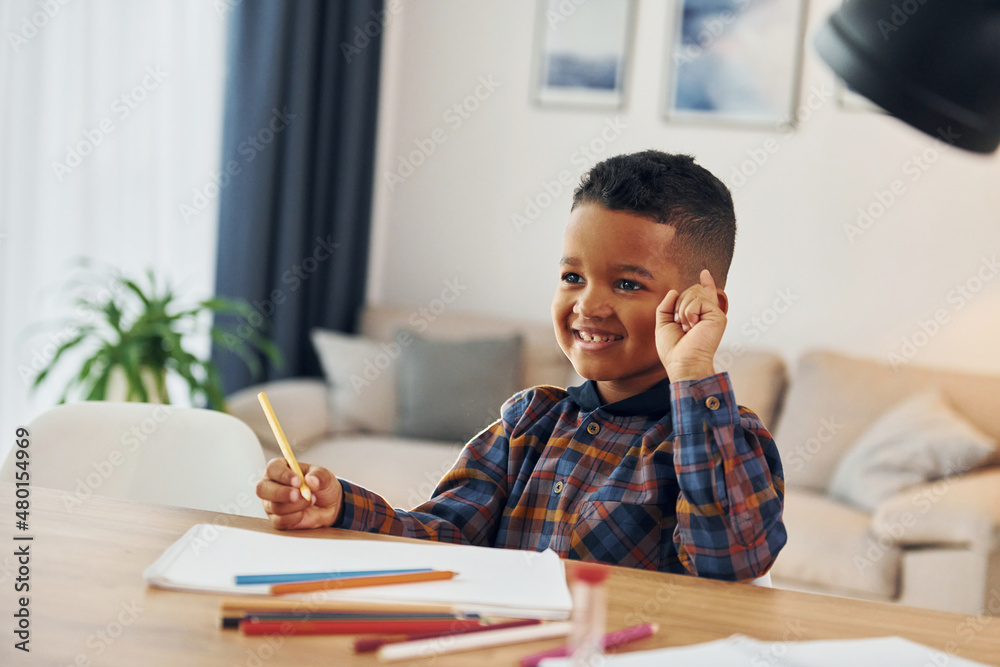Sitting by the table. Cheerful young boy is at home alone Sitting by the table. Cheerful young boy is at home alone