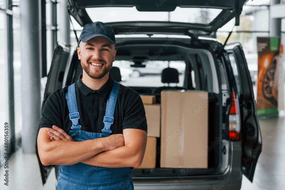 Work day. Delivery man in uniform is indoors with car and with order Work day. Delivery man in uniform is indoors with car and with order