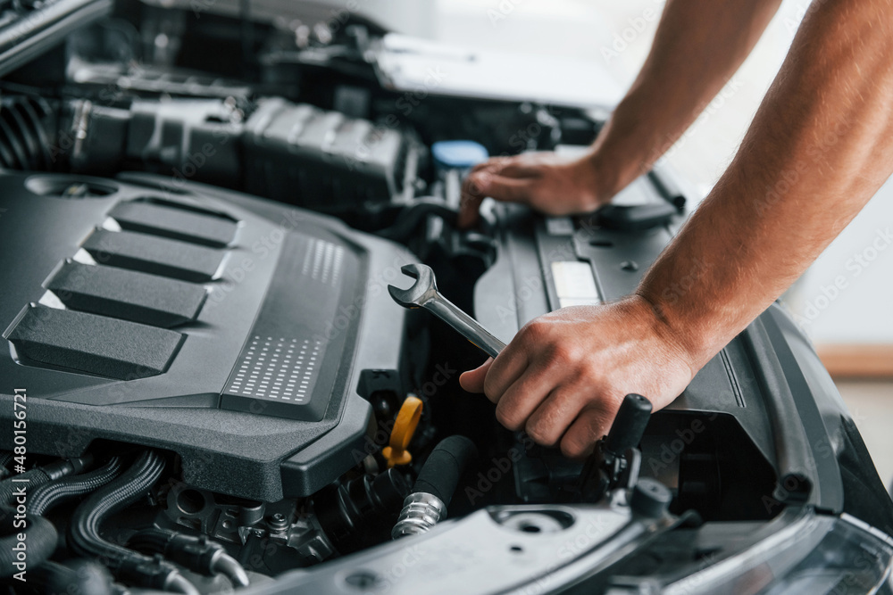 Some problems under the hood. Man in uniform is working in the autosalon at daytime Some problems under the hood. Man in uniform is working in the autosalon at daytime