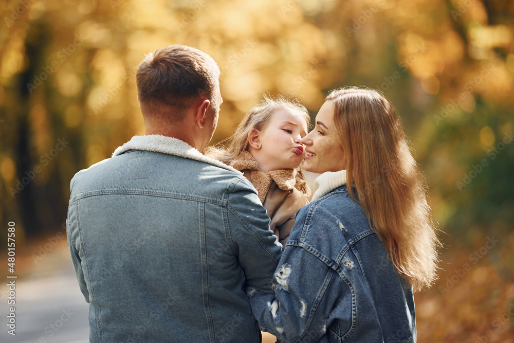 Little girl with her parents. Happy family is in the park at autumn time together Little girl with her parents. Happy family is in the park at autumn time together
