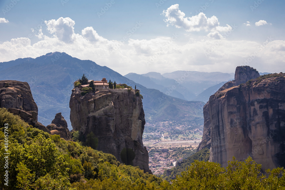 Beautiful scenic view of Orthodox Monastery of Áyios Ayía Triáda (Holy Trinity) on cliff, immense monolithic pillar, at the background of stone wall and rock formations of Meteora mountain, Greece.