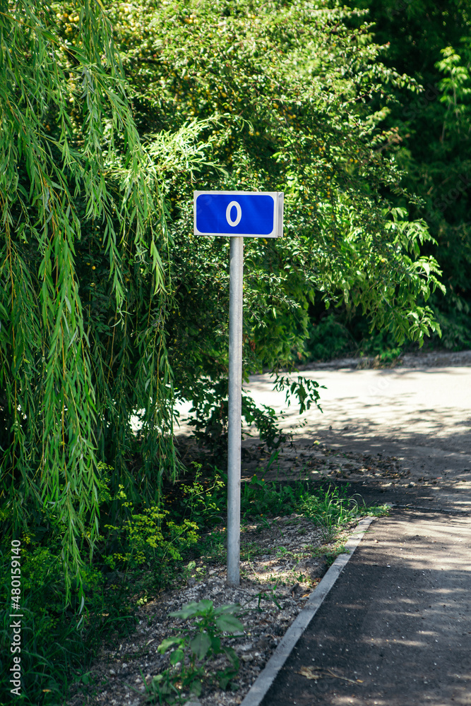 0 Zero kilometer road sign on the bystreet. Blue mark with information about mileage beginning of the path on green nature blur background. 0 Zero kilometer road sign on the bystreet. Blue mark with information about mileage beginning of the path on green nature blur background.