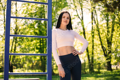 Girl female trainer ectomorph coach standing near horizontal bar, showing her beautiful body figure. Flexible female sporty model in the city park. 