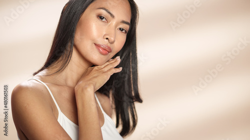 Female Beauty Portrait. Beautiful Asian Happy Brunette Woman Posing, Touching Her Face with Natural, Healthy Skin. Wellness and Skincare Concept on Soft Isolated Background. Close Up.