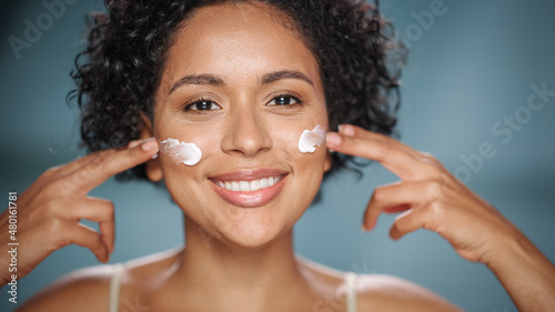 Female Beauty Portrait. Happy Black Multiethnic Brazilian Woman Touching Natural  Healthy Skin  Using Sunscreen  Applying Nourishing Face Cream. Cosmetics and Skincare Concept on Isolated Background.