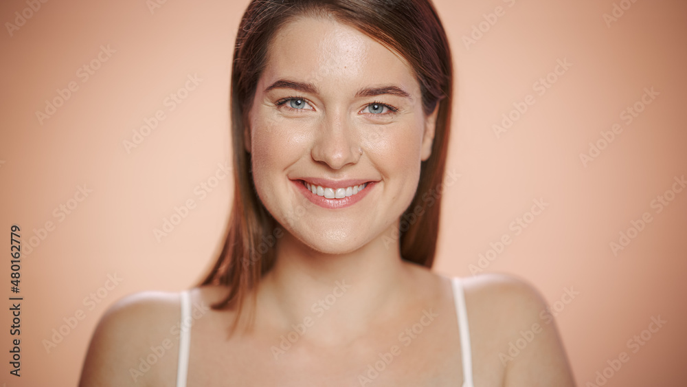 Close Up Female Beauty Portrait. Happy Caucasian Woman with Natural Healthy Skin, Brown Hair and Light Green Eyes Posing and Smiling. Wellness and Skincare Concept on Soft Isolated Background.