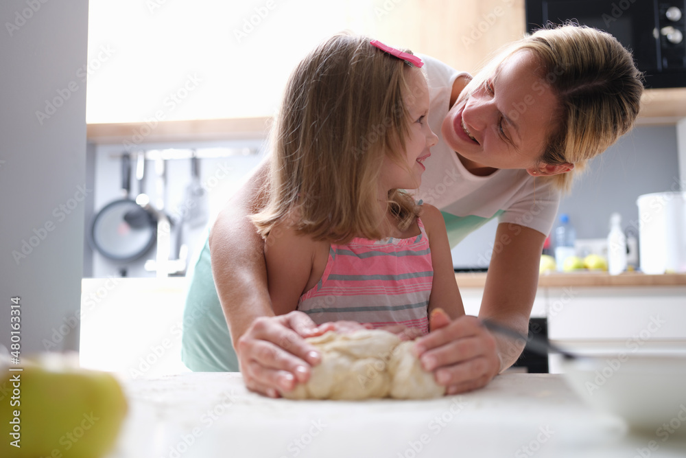 Mom and daughter knead dough together in the kitchen Mom and daughter knead dough together in the kitchen