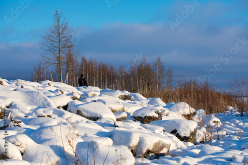 Man Walking in Winter. A man took a walk near a rocky pathway covered in snow during winter as the sun was shining brightly on a partly cloudy day.