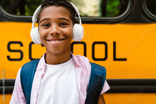 Papier peint Black boy in headphones smiling while standing by school bus