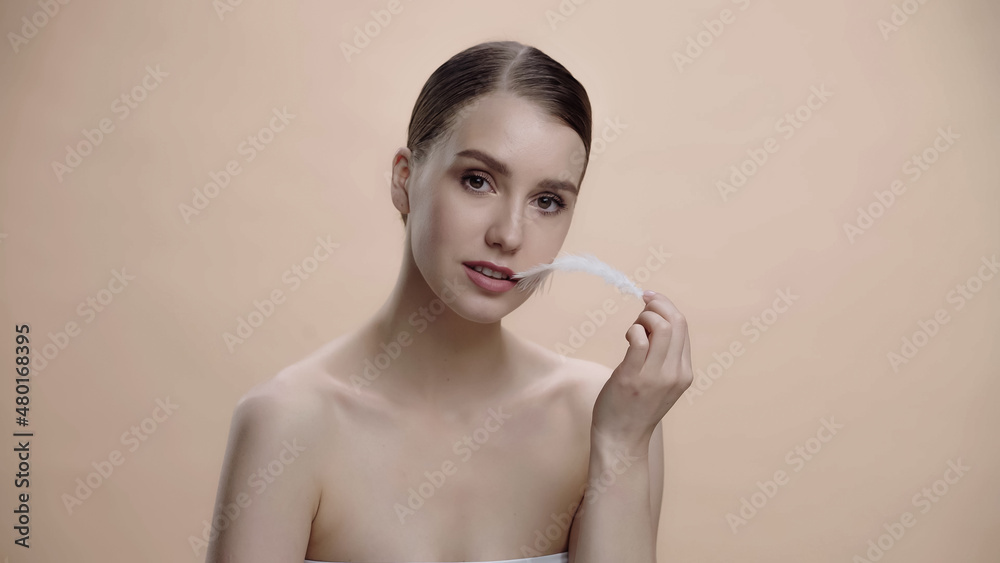 young woman with bare shoulders holding white feather isolated on beige. young woman with bare shoulders holding white feather isolated on beige.