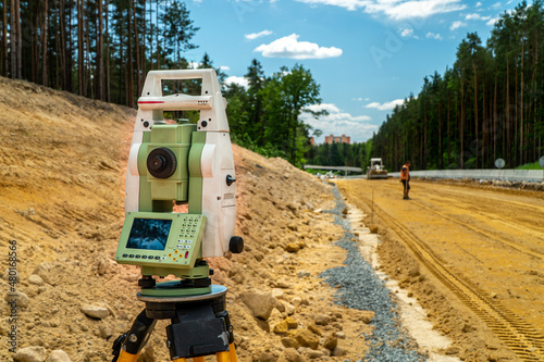 Surveyors equipment (theodolite or total positioning station) on the construction site of the road or building with construction machinery background