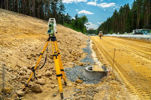 Surveyors equipment (theodolite or total positioning station) on the construction site of the road or building with construction machinery background