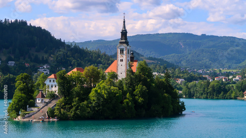 Closeup view of Catholic church situated on an island on Bled lake with mountains and villages on the background in the slovenian Alps