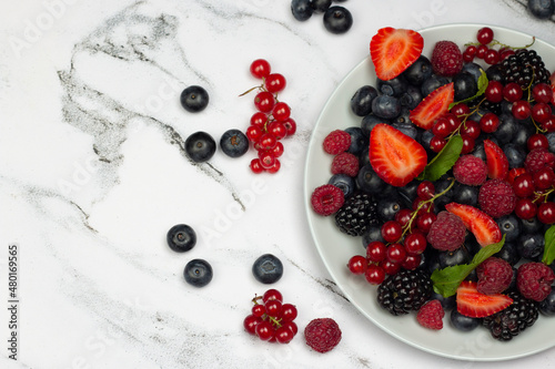 Summer berries salad. Plate of healthy fresh fruit salad: strawberry, blackberry, red currants, blueberry on white marble background.