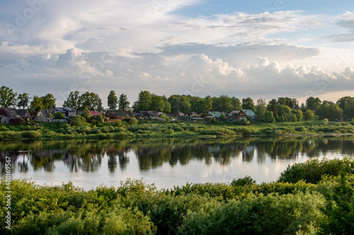 small village rivers landscape in the evening  with green trees, small houses on the coast, reflections on the water and  clouthy sky © OneLife_photography