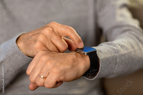 time, morning and people concept - close up of senior man hands with wristwatch or smartwatch at home