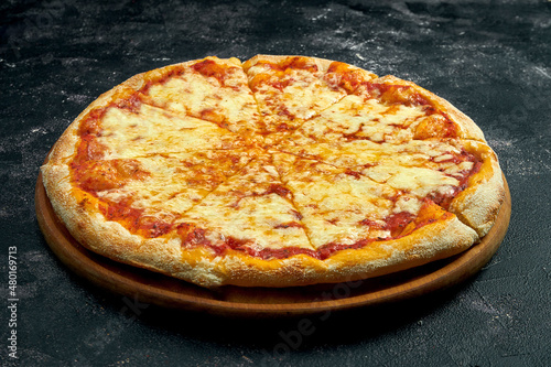Pizza with melted cheese on a black stone background. 45 degree angle view. Close-up, selective focus