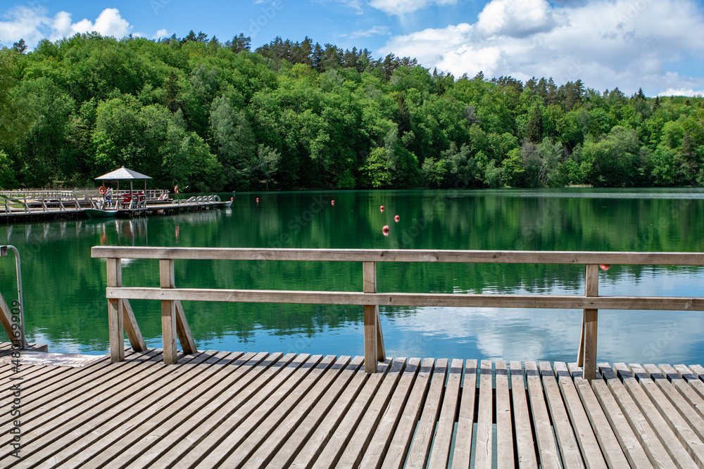 green water  lakes coast with wooden bridge, small house, juicy green trees and deep blue sky and clouths