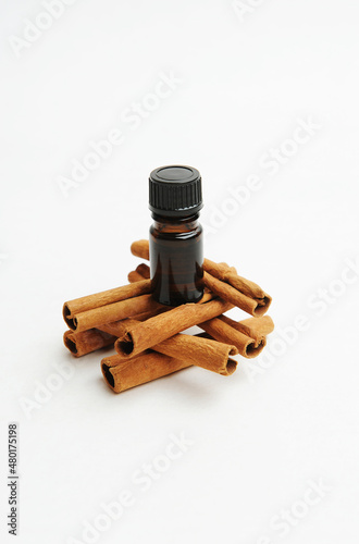 Small dark glass bottle on cinnamon sticks on white. Essential oil or extract. Cosmetic or food concept