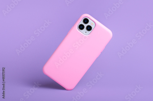 Smartphone iPhone 11 and 12 Pro max in pink silicone case falls down back view, phone case mockup isolated on purple background