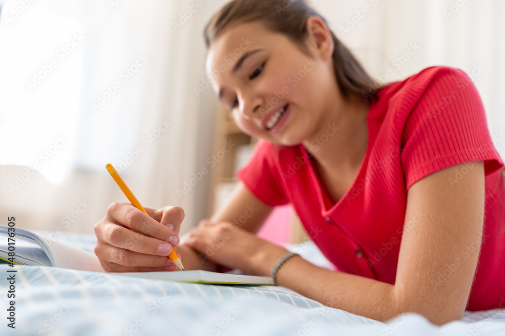 people and leisure concept - close up of happy smiling teenage girl with diary and pencil lying on bed at home people and leisure concept - close up of happy smiling teenage girl with diary and pencil lying on bed at home