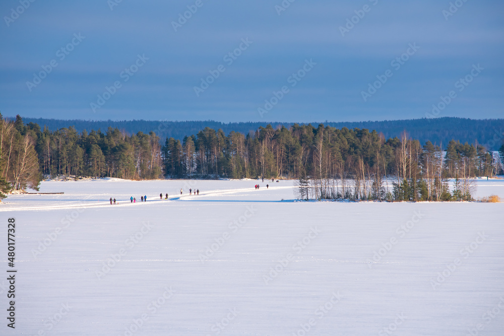 People Walking on the Frozen Lake. People followed the path made on the frozen lake on a cold but sunny winter day in Finland.