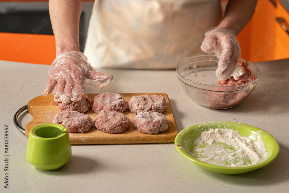 female hands in gloves form cutlets and roll them in flour 