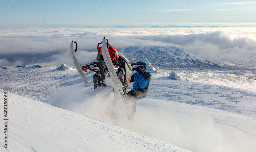 extreme driving of a mountain snowmobile. a sports snowmobiler in bright clothes and a helmet without brands, a colorful snowmobile of a new model. jumping with plumes and whirlwinds of snow extreme driving of a mountain snowmobile. a sports snowmobiler in bright clothes and a helmet without brands, a colorful snowmobile of a new model. jumping with plumes and whirlwinds of snow