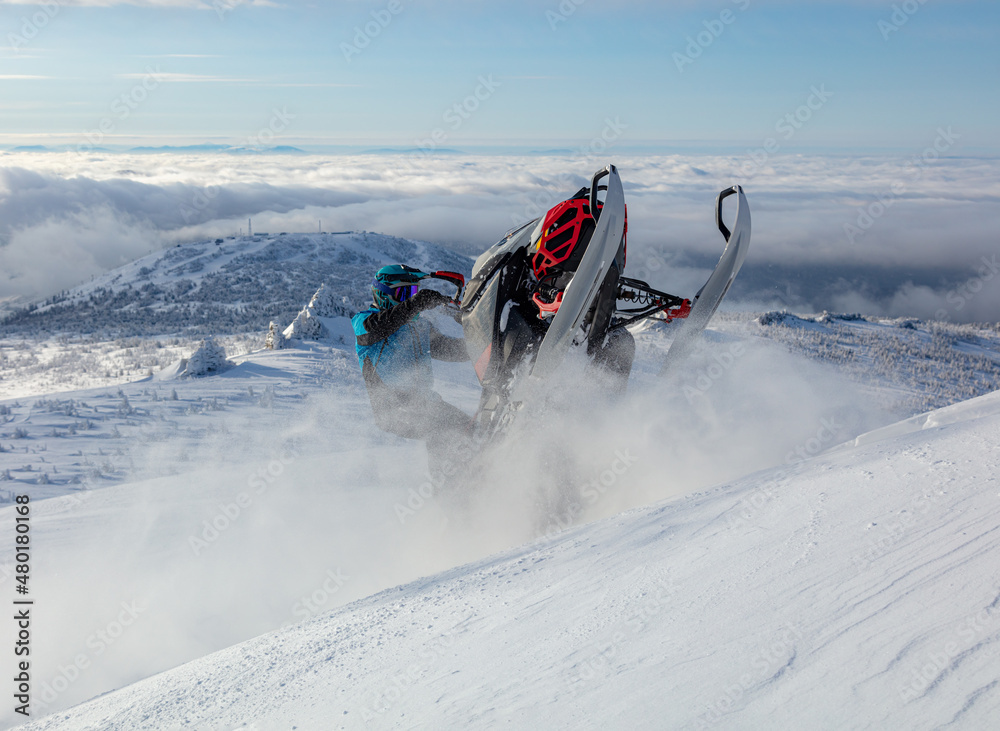 extreme driving of a mountain snowmobile. a sports snowmobiler in bright clothes and a helmet without brands, a colorful snowmobile of a new model. jumping with plumes and whirlwinds of snow extreme driving of a mountain snowmobile. a sports snowmobiler in bright clothes and a helmet without brands, a colorful snowmobile of a new model. jumping with plumes and whirlwinds of snow