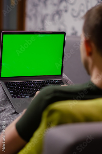 Caucasian man uses laptop with greenscreen of chromakey mockup. Person works, gets an education, does shopping online on personal computer. Green screen and chroma key. Freelance and mobility concept.